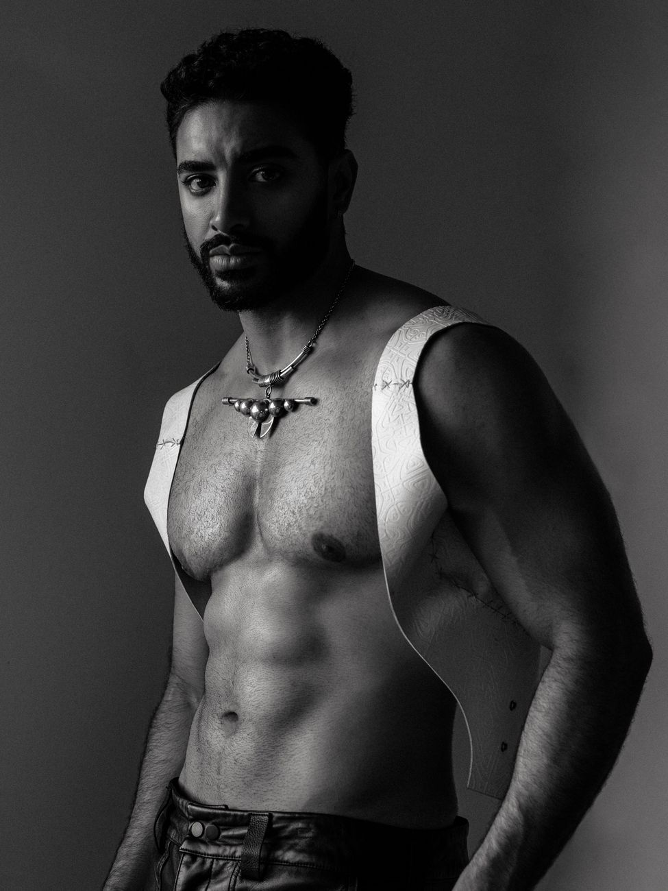 Menswear editorial: a leather harness worn over bare shoulders with a beaded collar, black and white