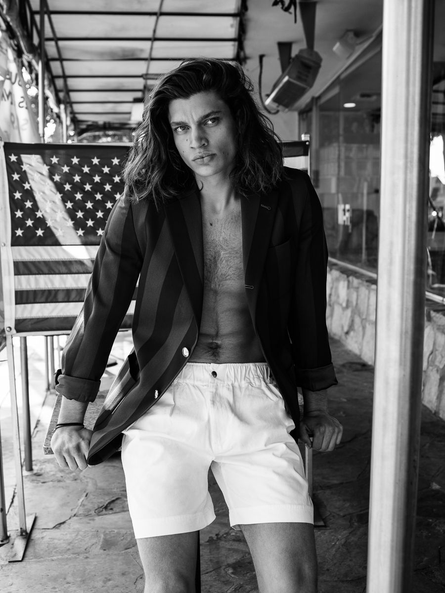 Strange Memories for JÓN Magazine: a striped blazer worn open with white shorts beneath an American flag, styled by Quentin Fears