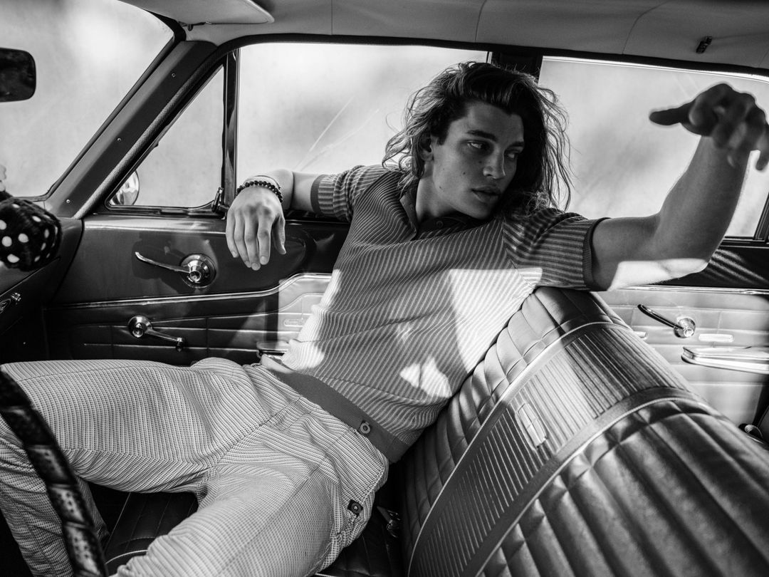 Strange Memories for JÓN Magazine: the model stretched across the bench seat of a vintage car in a striped knit and checked trousers, styled by Quentin Fears