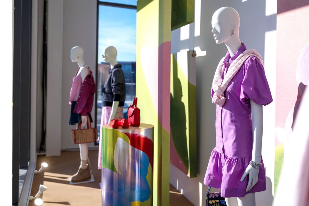 Spring Awakening window display: a violet puff-sleeve dress with a pink scarf beside a painted panel