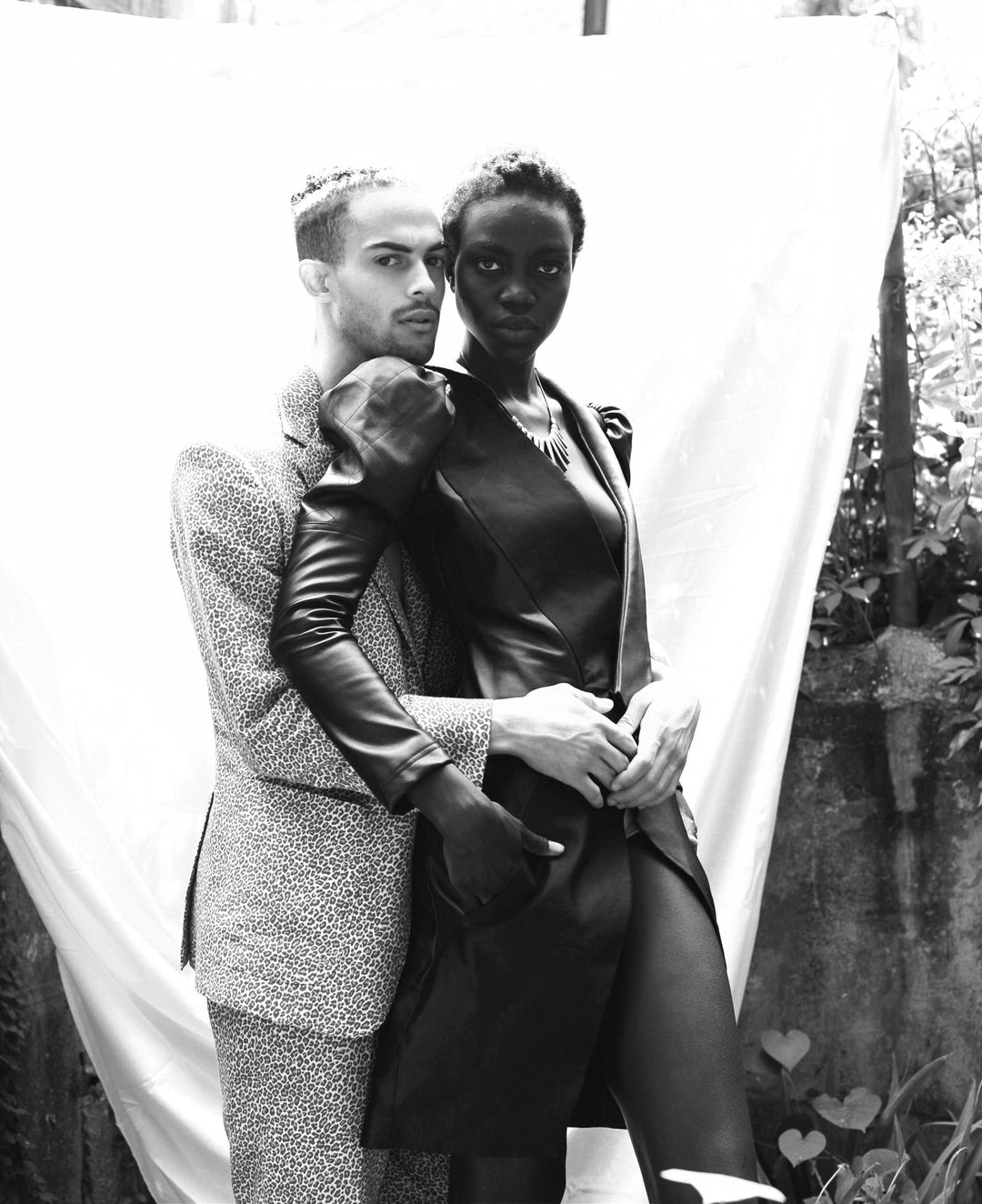 Visionarios Magazine editorial: two models in black and white, one in a leather coat with puffed shoulders, one in a leopard-print suit, against a hung white sheet