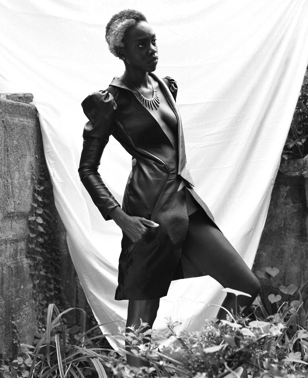 Visionarios Magazine editorial: a model in a long leather coat with puffed shoulders and a spiked necklace, turned in profile